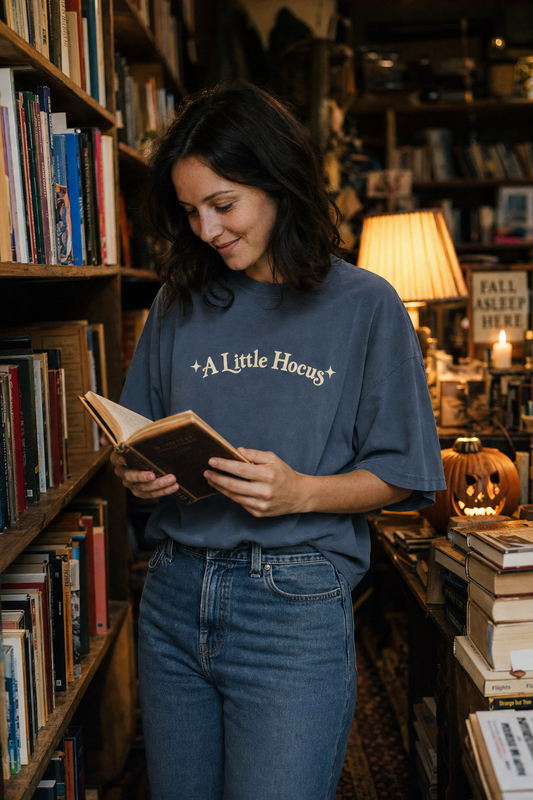 Woman in a second-hand bookshop wearing the faded indigo A Little Hocus oversized tee